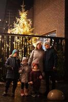madre con quattro bambini In piedi contro illuminato Natale albero all'aperto nel sera. foto