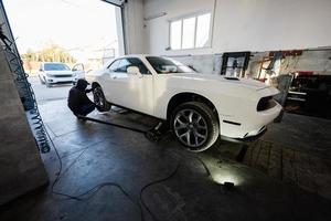 meccanico nel servizio riparazione stazione Lavorando con muscolo macchina. uomo lavoratore jack su il auto per diagnosticare il telaio. foto