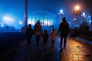 indietro di famiglia a piedi nel notte nebbioso città. foto