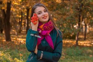 bellissimo ragazza nel un' rosa fazzoletto in giro il suo collo detiene rametto di Rowan nel mano e sorrisi foto