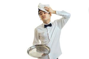 il giovane stanco Cameriere detiene un' vassoio e mettere un' tovagliolo su il suo testa foto