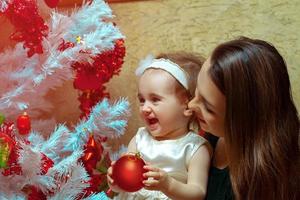 mamma con un' poco figlia decorare un' Natale albero e avendo divertimento foto