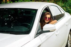 bellissimo sorridente ragazza nel occhiali da sole seduta nel il auto foto