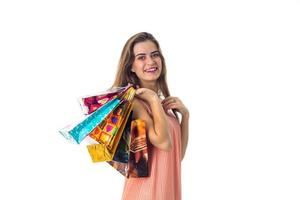 sorridente giovane ragazza mantiene su il suo spalla un' lotto di luminosa regalo pacchi, isolato bianca sfondo foto