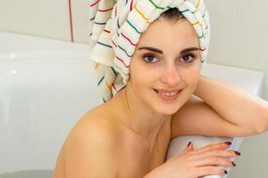 ragazza con asciugamano su sua testa sembra in il telecamera nel il bagno foto