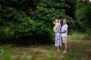 bellissimo giovane famiglia trasporto poco bambino figlia e sorrisi ogni altri a il verde parco foto