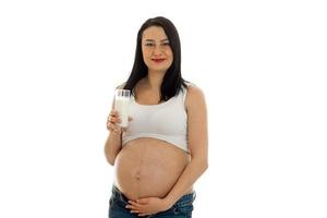 bella giovane incinta brunetta donna toccante sua pancia e bevande latti isolato su bianca sfondo foto