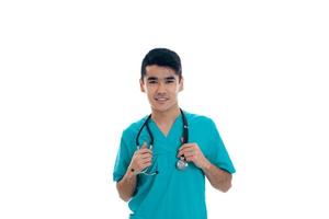 elegante giovane brunetta uomo medico nel blu uniforme con stetoscopio in posa isolato su bianca sfondo foto