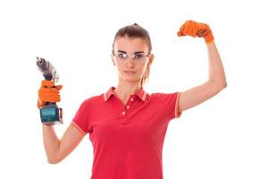 bellezza giovane brunetta costruttore ragazza nel uniforme e bicchieri fa rinnovamento con trapano nel mani isolato su bianca sfondo foto