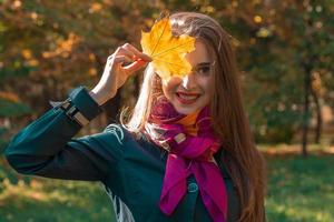 giovane carino ragazza è sorridente e Tenere un' foglio vicino il occhio avvicinamento foto