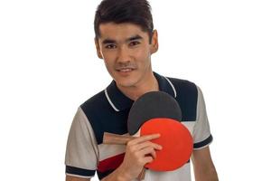 un' giovane uomo detiene nel il suo mano racchette per tavolo tennis e un' avvicinamento di un' sorridente isolato su bianca sfondo foto