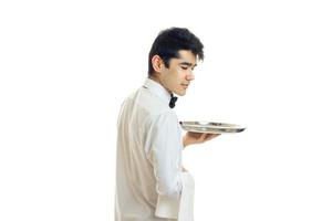 giovane carino Cameriere nel un' bianca camicia sta lateralmente e Tenere un' vassoio foto