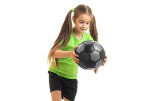 carino poco ragazza nel verde uniforme con calcio palla nel mani foto