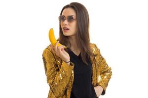 bellissimo fascino ragazza nel il giro spettacoli nel il oro giacca mantiene il Banana nel mano foto