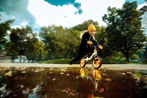 carino poco ragazza cavalcate attraverso il pozzanghere su bicicletta a il parco foto