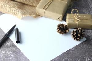 vacanze i regali. Natale e nuovo anno.regalo scatola avvolto nel Marrone carta pino coni e bianca carta e penne posto su il tavolo, copia spazio. foto