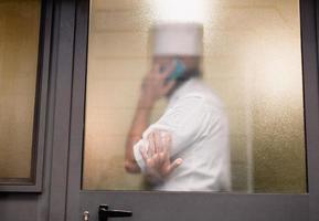 silhouette dietro a il bicchiere di un' uomo nel un' dello chef uniforme parlando su il Telefono. foto