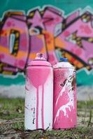 un' pochi Usato dipingere lattine menzogna su il terra vicino il parete con un' bellissimo graffiti pittura nel rosa e verde colori. strada arte concetto foto