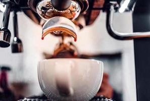 vicino su di caffè far cadere estrazione a partire dal il caffè macchina con un' portafilter scrosciante caffè in un' tazza, caffè espresso scrosciante a partire dal caffè macchina a il caffè negozio foto