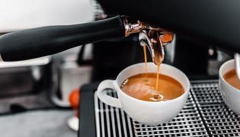 caffè estrazione a partire dal il caffè macchina con un' portafilter scrosciante caffè in un' tazza, espresso poro a partire dal caffè macchina a caffè negozio foto