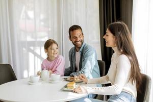 felice giovane famiglia mangiare dolci e bere il tè insieme foto