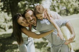 giovane famiglia felice con la piccola figlia carina che si diverte nel parco in una giornata di sole foto