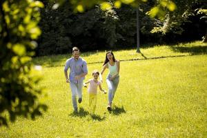 giovane famiglia felice con la piccola figlia carina che corre nel parco in una giornata di sole foto