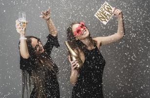 Due femmina amici festeggiare nuovo anno con coriandoli e Champagne Tenere cartello. isolato foto