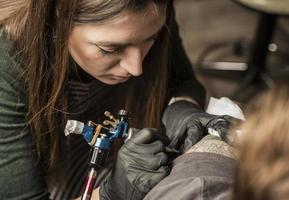 vicino su tatuaggio macchina. donna la creazione di immagine su mano con esso nel salone foto