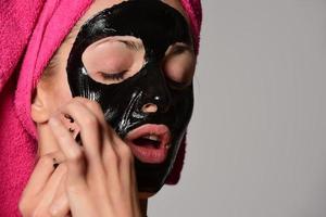 bellissimo femmina modello con nero facciale cosmetico maschera. isolato su grigio sfondo foto