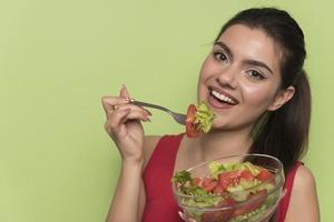 ritratto di un' contento giocoso ragazza mangiare fresco insalata a partire dal un' ciotola foto