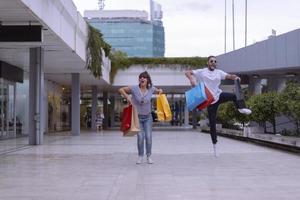 ritratto di allegro caucasico giovane coppia uomo e donna Tenere molti carta borse dopo shopping mentre a piedi e parlando su strada. contento famiglia coppia con pacchi all'aperto. acquisto concetto foto