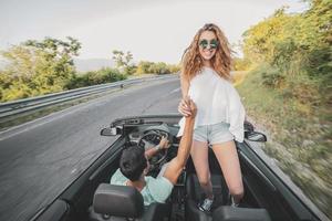 amici avendo divertimento a auto viaggio in giro il mondo. coppia nel amore con braccia su su un' convertibile macchina. foto