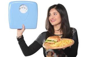 ritratto di un' bellissimo divertente giovane ragazza su il bianca sfondo, Tenere un' vassoio hamburger con Hamburger e misurazione scala foto