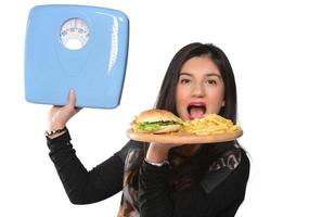 ritratto di un' bellissimo divertente giovane ragazza su il bianca sfondo, Tenere un' vassoio hamburger con Hamburger e misurazione scala foto