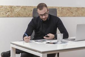 giovane uomo d'affari che lavora a casa con laptop e documenti sulla scrivania foto