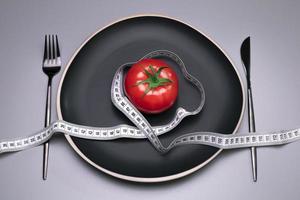 pomodoro e misurazione nastro su il piatto. il concetto di dieta. foto