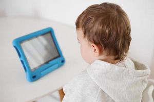 contento poco ragazzo giocando gioco su digitale tavoletta a casa. ritratto di un' bambino a casa Guardando cartone animato su il tavoletta. moderno ragazzo e formazione scolastica tecnologia. foto