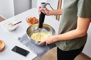 donna nel cucina cucinando un' torta. mani battere il Impasto con un elettrico miscelatore foto