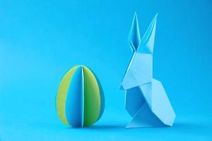 carta origami esater coniglio e colorato uovo su il blu sfondo foto