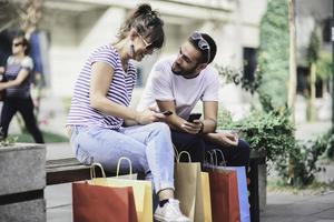 ritratto di allegro caucasico giovane coppia uomo e donna Tenere molti carta borse dopo shopping mentre a piedi e parlando su strada. contento famiglia coppia con pacchi all'aperto. acquisto concetto foto