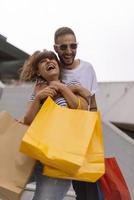 ritratto di allegro caucasico giovane coppia uomo e donna Tenere molti carta borse dopo shopping mentre a piedi e parlando su strada. contento famiglia coppia con pacchi all'aperto. acquisto concetto foto