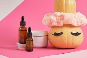 finto su impostato di cosmetico contenitori e zucca con fascia per capelli e falso ciglia su rosa sfondo foto