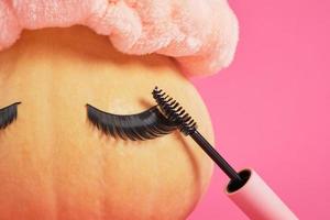 mascara nel finto su vuoto rosa confezione e zucca con falso ciglia su rosa sfondo copia spazio foto