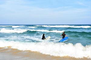 surfers coppia in attesa per il alto onde su spiaggia - sportivo persone con Surf tavole su il spiaggia - estremo sport e vacanza concetto foto