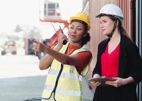 diverso persone godere Lavorando insieme a contenitore cortile. industriale ingegnere donna e femmina caposquadra indossare sicurezza elmetto protettivo siamo guardare inoltrare a carico distribuzione. diversità attività commerciale persone concetto foto