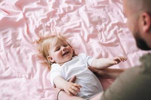 contento padre giovane uomo e bambino ragazza poco figlia avendo divertimento su letto nel camera a casa foto