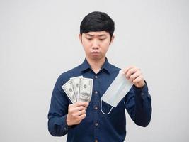 asiatico uomo guardare a i soldi e proteggere maschera nel il suo mano sensazione confuso su bianca sfondo foto