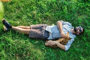 superiore Visualizza di uomo e cane dire bugie su verde erba. attraente europeo uomo è abbracciare il suo cane. foto