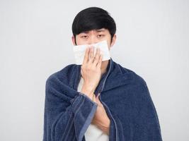 asiatico uomo vicino fazzoletto di carta a il suo naso sensazione malato e copertina il suo corpo di asciugamano ritratto foto